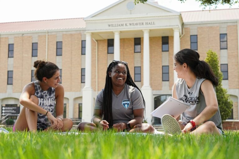 Three female students engaged in conversation on a college campus.​