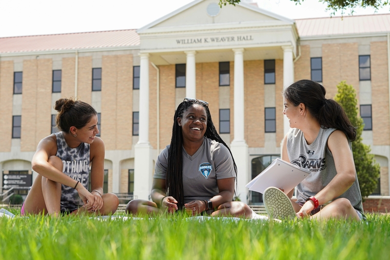 Three female students engaged in conversation on a college campus.