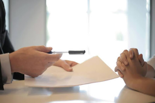 One person handing a pen and paper to another.
