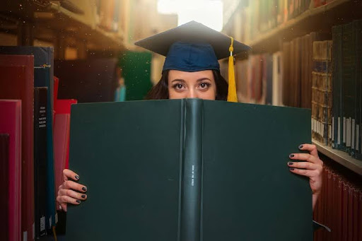 Woman in graduation gown and cap holding a large book