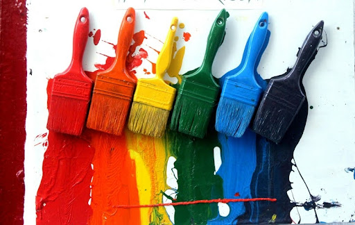 Four paintbrushes dipped in red, yellow, blue, and green paint.