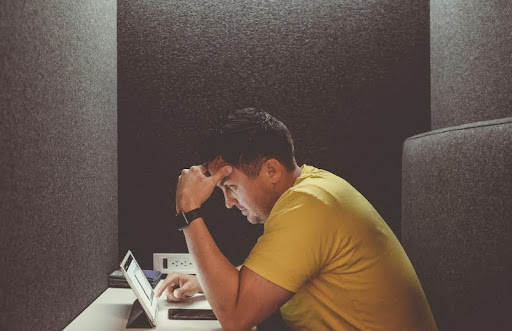 Man sitting at desk looking overwhelmed while working on laptop.