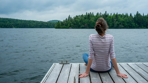 Woman sitting alone on a dock, looking out over calm water.
