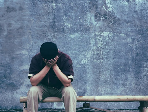 Man sitting alone on a bench, looking down in thought.