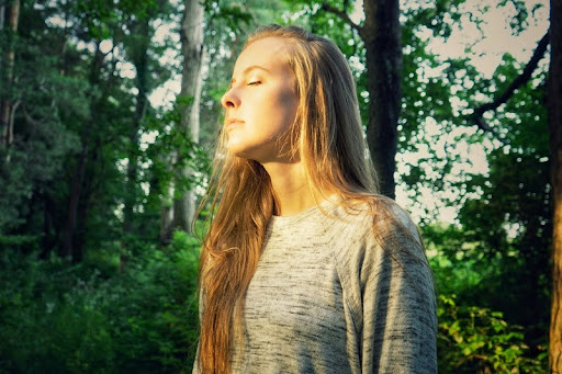 Woman walking near green trees, deep in thought