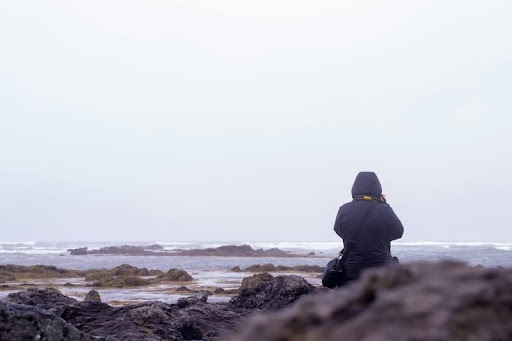 Person in black sitting alone on a rock by the sea