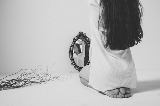 Woman sitting on a bed looking at her reflection in a mirror