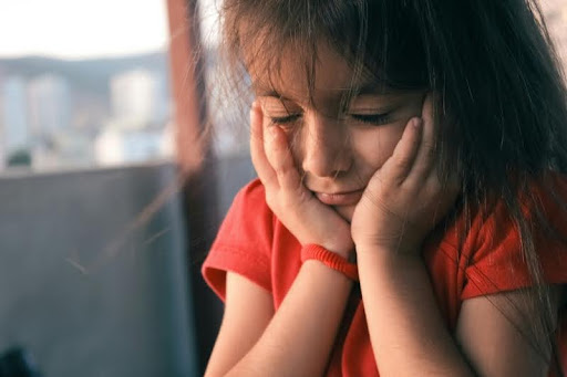 Young girl holding her face in her hands, looking down