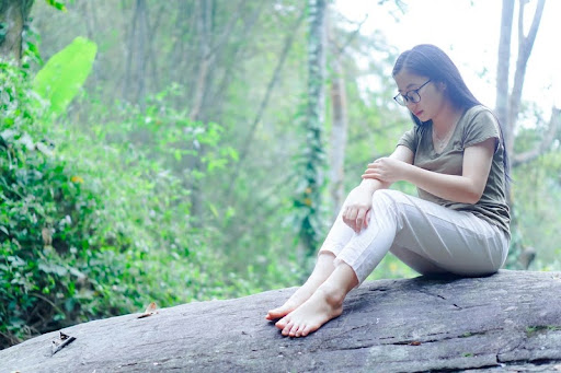 Woman sitting alone on a rock in the woods, surrounded by trees.