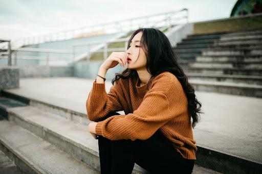Woman sitting alone on a sidewalk, looking thoughtful.