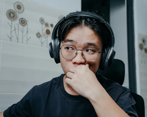 Man wearing glasses and headphones, staring off in thought.