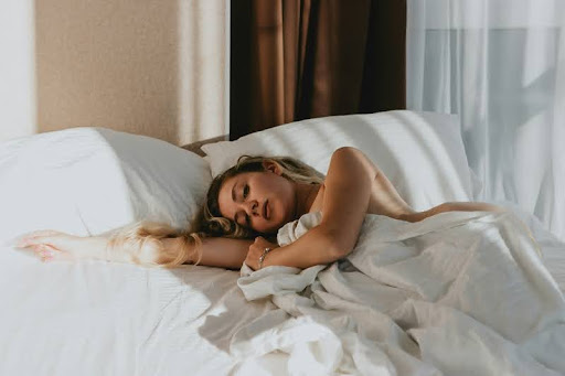 Woman resting in bed, wrapped in a blanket, facing away