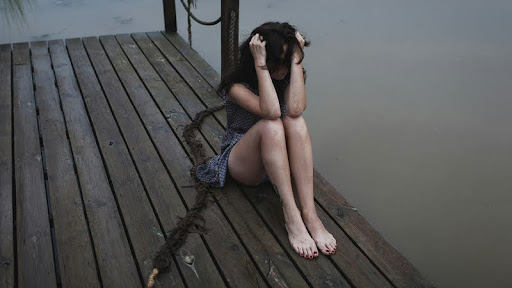 Woman sitting alone on a dock with her head in her hands