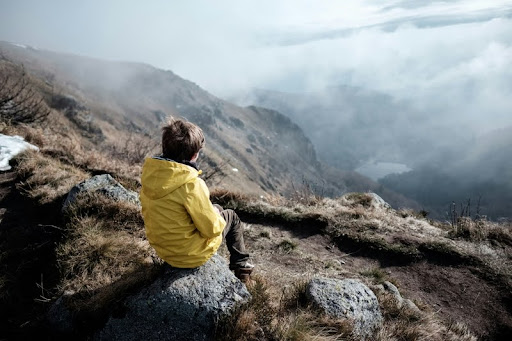 Person sitting on a mountaintop overlooking a peaceful valley