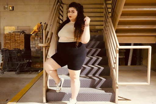 Woman in shorts standing on stairs, looking confident and thoughtful.