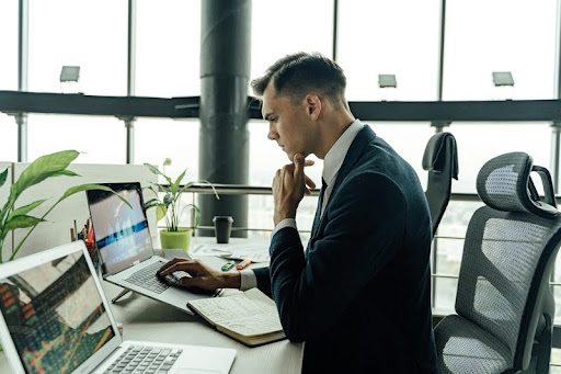 Man in a suit using a laptop in an office, looking thoughtful.
