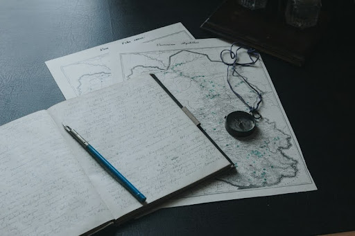 Book, pen, and map laid out on a wooden table.