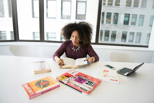 Woman reading a book with a laptop on the table