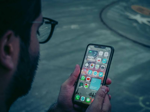 Person holding a smartphone showing a variety of app icons on the screen.