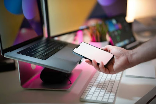 Person holding a smartphone with a laptop open on a desk