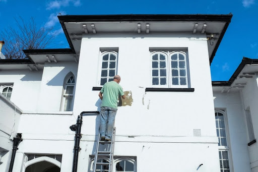 Man on ladder repairing exterior siding of a white house