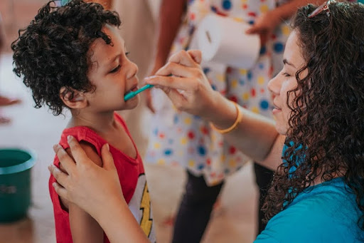 Mother helping her child brush their teeth during the morning routine.