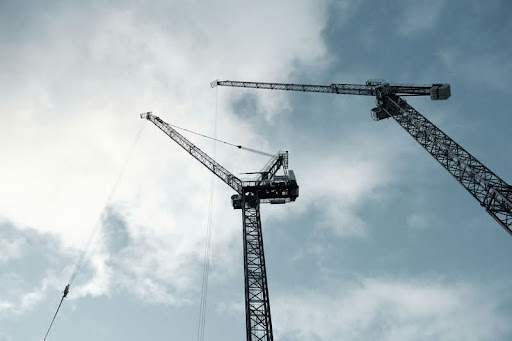 Black construction cranes set against a cloudy daytime sky.