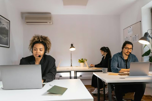Three people working individually on laptops at separate desks in a quiet room.