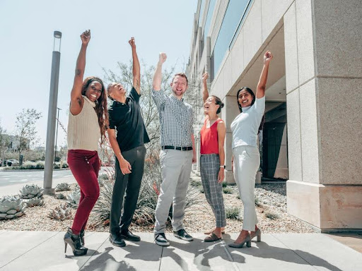 Group of diverse coworkers standing in a field, cheering and celebrating together.