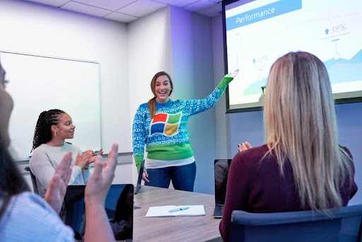 Woman presenting to a group, pointing at a projector screen.