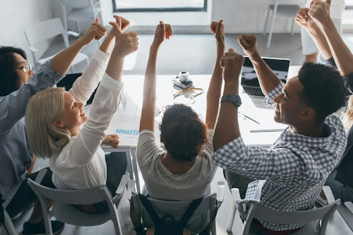 Colleagues in an office raising their hands together in unity and celebration