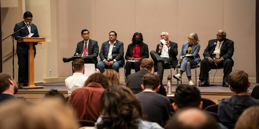 Panel of speakers seated on a stage facing a live audience.