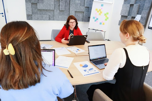 Three white women having a discussion in a modern office setting.