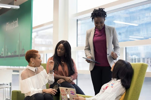 Four professional women having a conversation in an office setting.