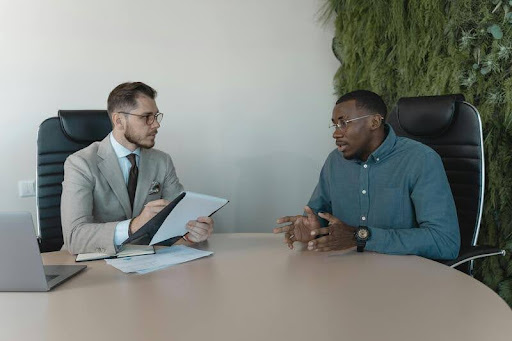 Man in blue shirt discussing documents with man in suit in an office setting.