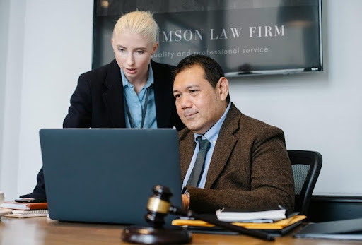 Senior man in a suit and woman standing beside him reviewing something on a laptop.