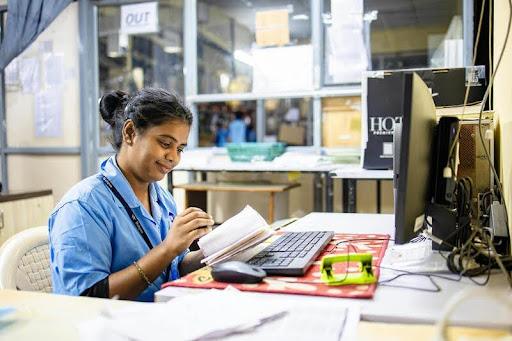 Busy woman working at a desk in an office surrounded by paperwork and a laptop.