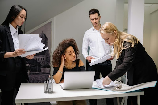 Four coworkers reviewing documents around a table with a laptop.