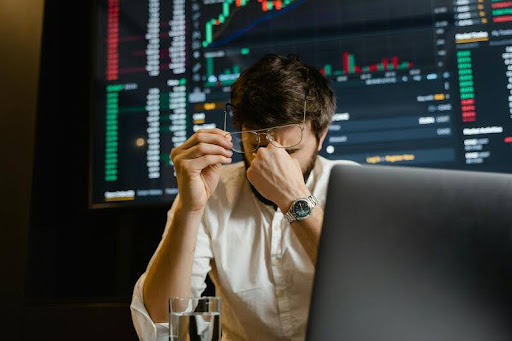 Man in a white shirt holding his head while looking at his laptop in an office.