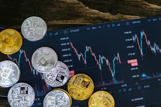 Close-up of silver and gold cryptocurrency coins in front of a computer screen with crypto data.