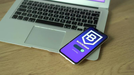 Phone resting on laptop, both displaying a blockchain application interface.