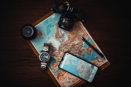Phone, map, watch, and camera arranged on a table.