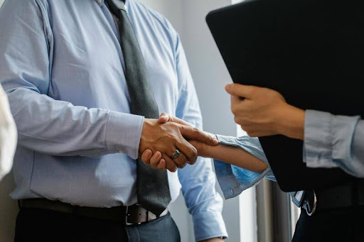 Man greeting a woman with a handshake in a modern office.