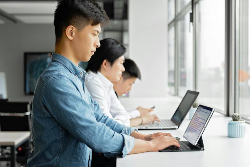 Three people working on laptops in a modern office.