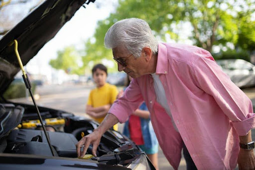 Elderly man working under the hood of his car outdoors.