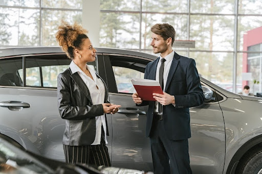 Woman standing next to a car while signing purchase documents at a dealership
