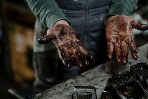 Mechanic's hands covered in motor oil while working on a car engine.