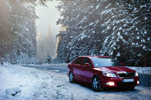 Car driving on a snow-covered road surrounded by winter trees.