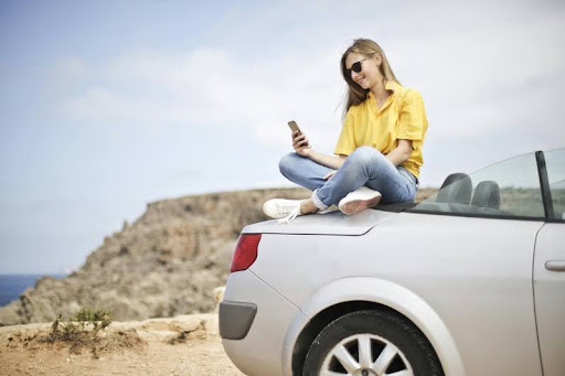 Woman sitting on the hood of a car, smiling confidently.