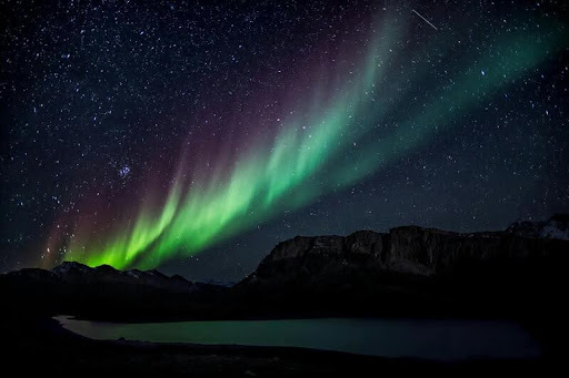 Northern lights glowing in the night sky above a dark landscape